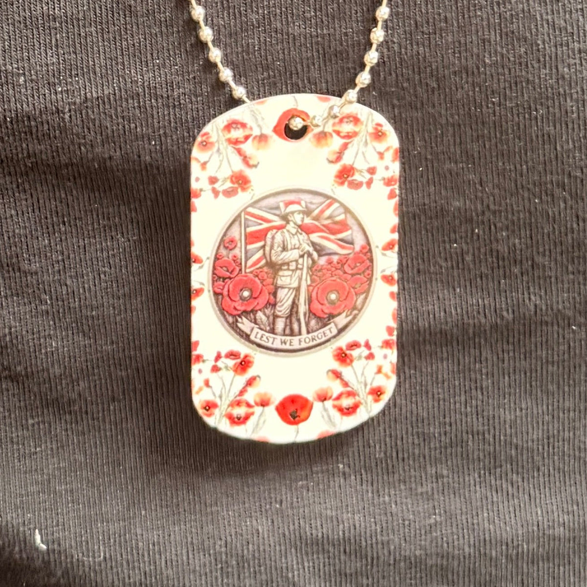 ID tag necklace with a red poppy remembrance design, shown worn on a dark top.